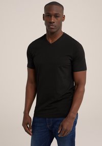 Tricou negru cu decolteu în V, confecționat dintr-un material moale, cu o croială ajustată și mâneci scurte, textură fină, purtat cu blugi albaștri.