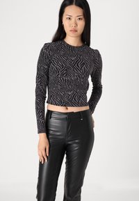 Zwarte langemouwen crop top met een getextureerd zebra-streep patroon, gecombineerd met hoge zwarte nepleren broek.