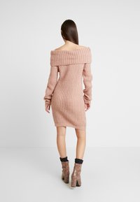 Hellrosa schulterfreies Strickkleid mit gerippter Struktur und langen Ärmeln, kombiniert mit Stiefeletten im Schlangenledermuster.