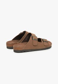 Bruine sandalen met een voetbed, voorzien van gespaccenten, gemaakt van zacht materiaal, met een kurken zool en een open teen ontwerp. Textuurdetails zijn zichtbaar.