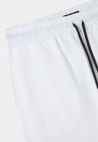 Pantaloni della tuta bianchi in cotone con vita elasticizzata, dotati di lacci neri e tasche laterali, texture liscia e design casual.