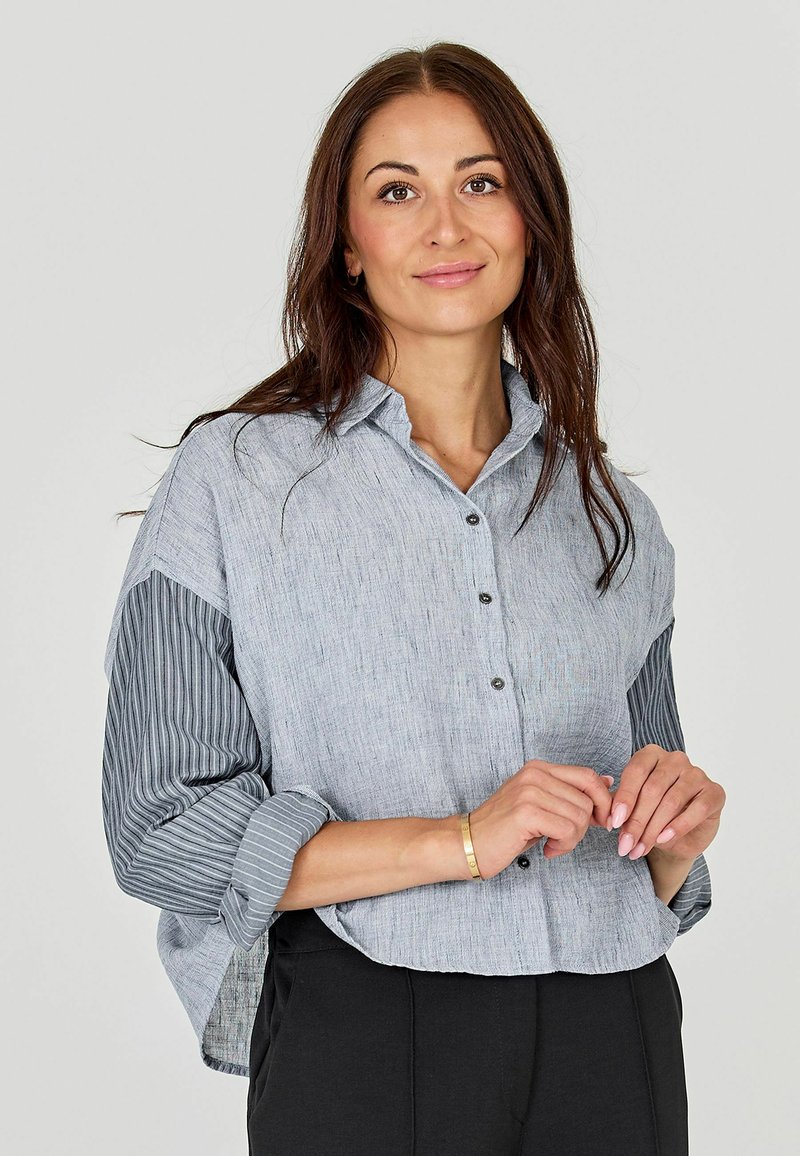 Light blue button-up shirt with a textured front, striped sleeves, and a relaxed fit. Features a classic collar and rolled sleeves.