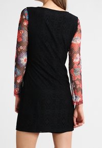 Vestido negro con mangas de encaje floral. Las mangas transparentes y texturizadas presentan coloridos patrones florales. La parte del cuerpo tiene un acabado sólido y suave.