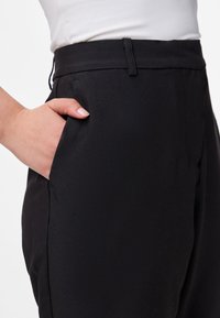 Calças pretas ajustadas com uma textura suave, apresentando um bolso lateral e um cós estruturado, apropriadas para várias ocasiões.