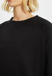 Schwarzer Sweatshirt mit Rundhalsausschnitt und Raglanärmeln, aus glattem Stoff gefertigt, mit lockerer Passform und ohne sichtbare Muster oder Akzente.