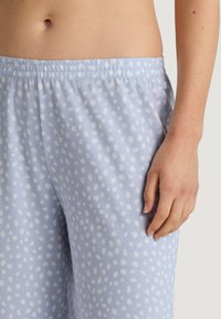 Light blue pajama pants in soft fabric with white polka dots, featuring an elastic waistband and side pockets.