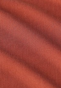 Tissu texturé dans une couleur terracotta chaude, présentant un motif tissé lisse avec des vagues subtiles, créant une apparence douce et flexible.
