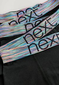 Svarta leggings med ett färgglatt randigt midjeband som har ordet "next" i svart. Texturen är slät och sömmarna är synliga längs kanterna.