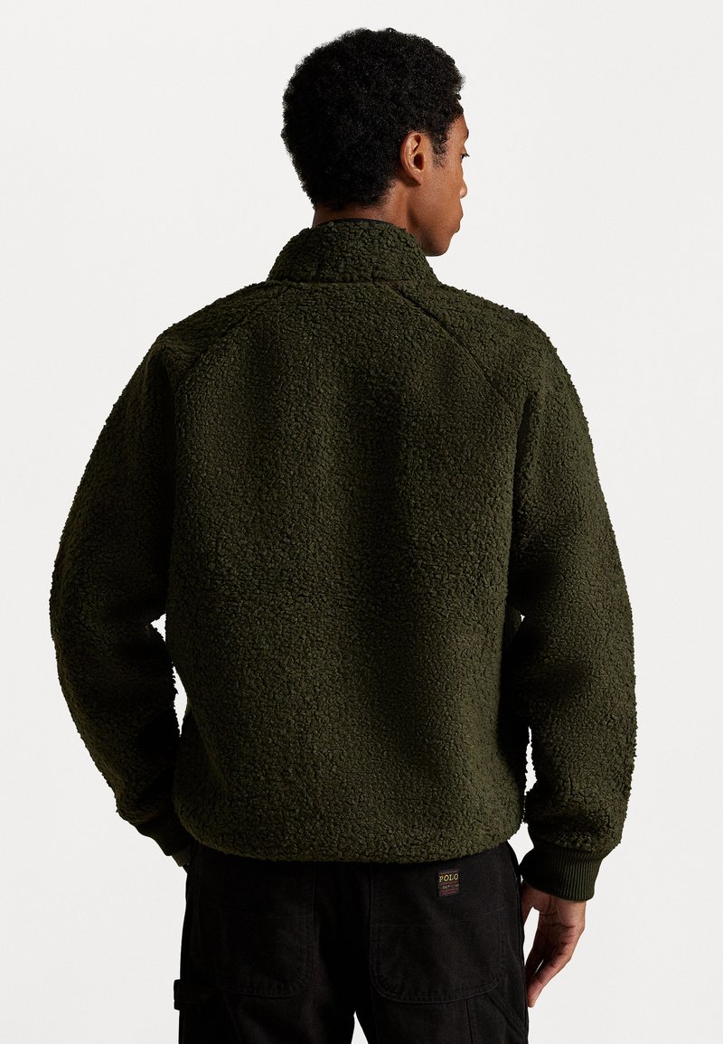 Grüner Fleece-Pullover mit hohem Kragen, strukturierten Oberflächen und gerippten Bündchen. Die Rückseite zeigt eine lockere Passform und Nahtdetails.