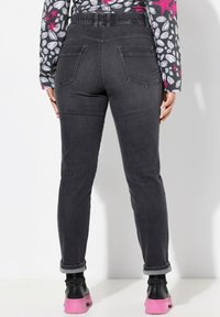 Jeans de denim negro con cintura alta, corte recto y puños doblados. Cuenta con dos bolsillos traseros y una textura suave.