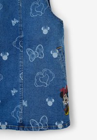 Tejido de denim con contornos blancos de lazos, guantes y cabezas de Mickey Mouse, que presenta un gráfico a color de Minnie Mouse cerca del dobladillo.