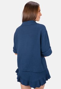 Ensemble de détente en tissu tissé bleu marine comprenant une chemise à col avec des manches retroussées et une jupe à ourlet volanté, offrant une apparence texturée.