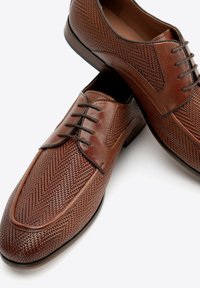 Zapatos de cuero marrón con textura trenzada, con punta redonda y cordones, diseñados con costuras de contraste y un borde liso.