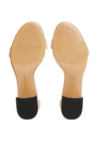 Paire de sandales beiges à semelles plates avec des patchs noirs texturés au talon, nom de marque visible "Tommy Hilfiger" sur les semelles.
