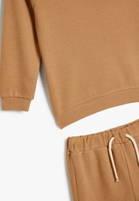 Brun texturerad sweatshirt med ribbade ärmar och matchande joggers med dragsko. Båda plaggen har en slät yta och en avslappnad passform.