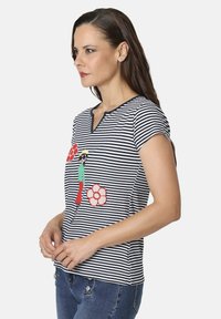 Camiseta de manga corta a rayas con cuello en V, que presenta un diseño bordado de una figura y flores en rojo, blanco y verde sobre un fondo azul marino.