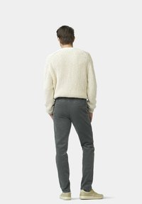 Beige gestrickter Pullover mit einem strukturierten Design, kombiniert mit grauen Cordhosen und hellbeigen Sneakers. Ansicht von hinten.