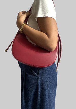 Borsa a tracolla in pelle rossa con una texture liscia, forma semi-circolare e cinturini regolabili. Dettagli in metallo dorato sugli estremi delle cinghie.