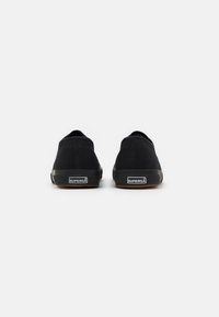 Scarpe slip-on nere in tela con suola in gomma. Presentano una parte superiore testurizzata, un retro arrotondato e un'etichetta con il marchio sul tallone.