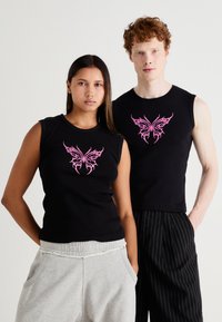 Black sleeveless tops featuring a pink butterfly graphic at the center, worn with gray sweatpants and pinstriped trousers. Smooth fabric.
