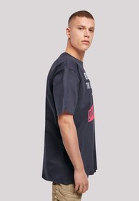 Navy blue cotton t-shirt with short sleeves, featuring white and pink text on the front. Relaxed fit and crew neckline.
