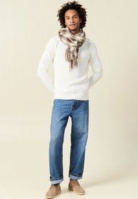 Maglione a coste bianco, jeans blu e stivali alla caviglia beige. Una grande sciarpa decorata in beige e marrone con frange avvolta attorno al collo.