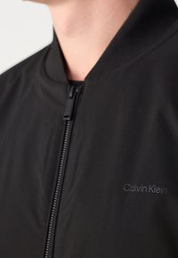 Schwarze Bomberjacke mit Reißverschluss, geripptem Kragen und dezentem „Calvin Klein“-Logo in einem eleganten, minimalistischen Design.