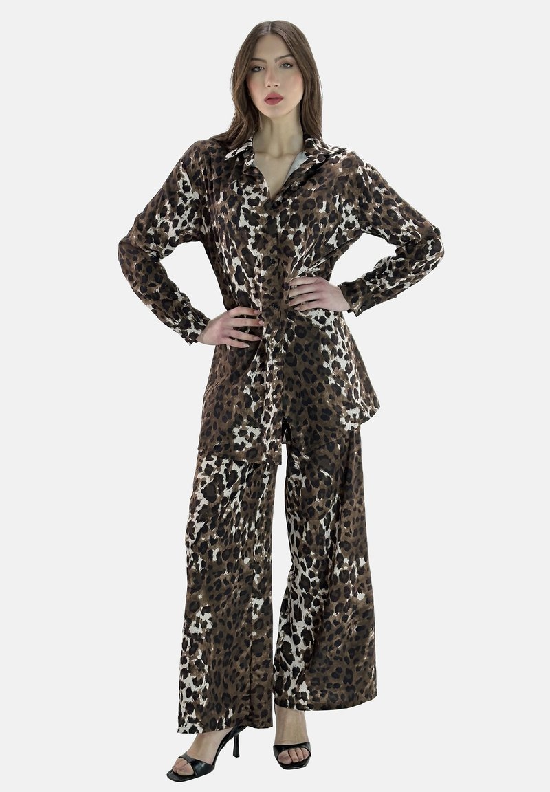 Outfit con stampa leopardata realizzato in tessuto morbido; presenta una camicia con bottoni e pantaloni a gamba larga in marrone, crema e nero con una finitura lucida.