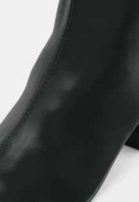 Κοντινό πλάνο μαύρου δερμάτινου μποτάκι αστραγάλου που δείχνει την ομαλή υφή και τις λεπτομερείς ραφές κατά μήκος της πλευράς.