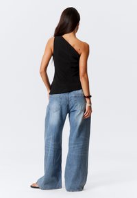 Asymmetrisches schwarzes Top mit figurbetontem Design, getragen mit weit geschnittenen hellblauen Jeans. Glatte Textur, minimale Details, entspannter Schnitt.