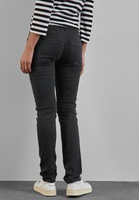 Svarta skinny jeans med en standard midja, bakfickor och en jämn textur, i kombination med vita sneakers och en randig topp.