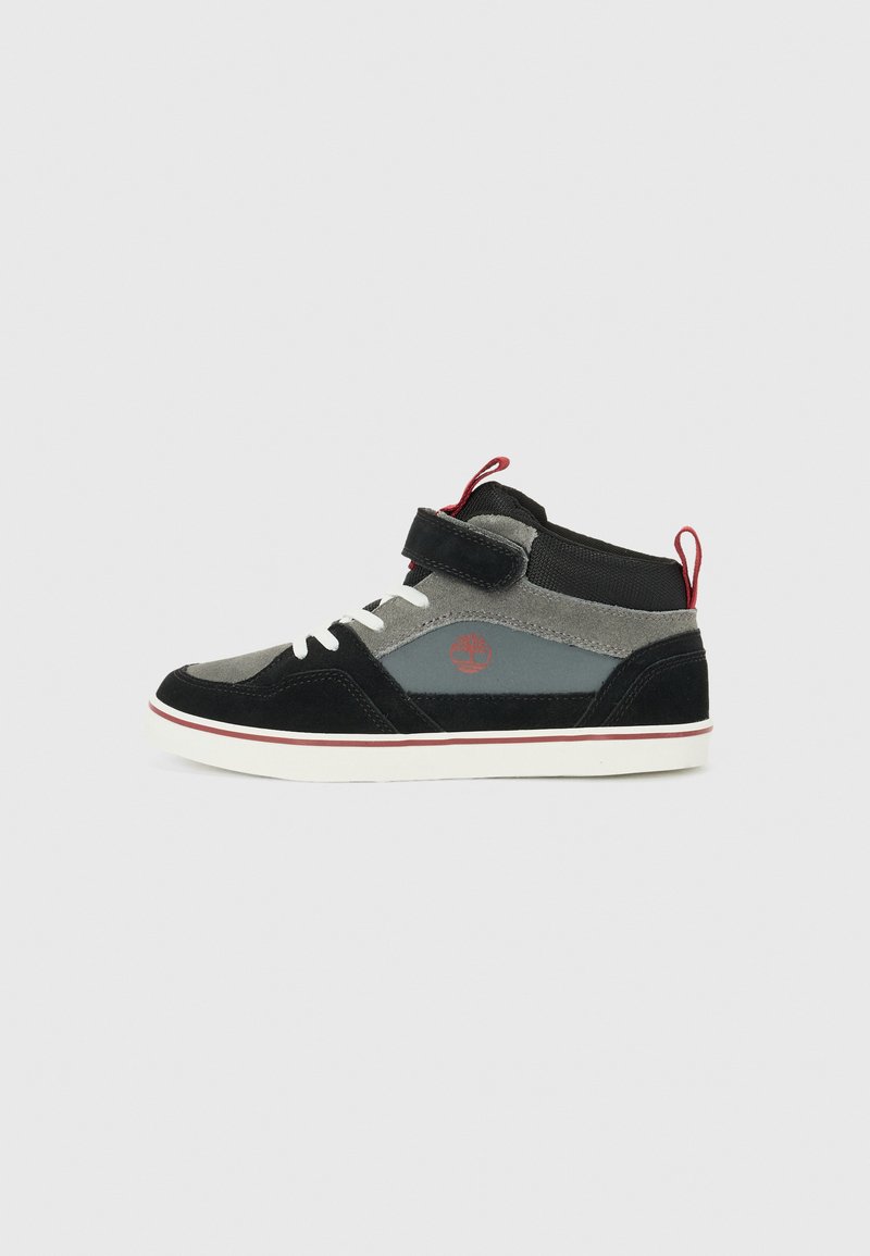 High-top sneaker in black and gray suede, featuring a Velcro strap, white lace, red accents, and a rubber sole with a contrasting edge.