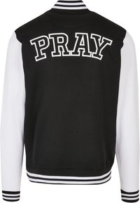 Giacca varsity bianca e nera con la scritta "PRAY" in grassetto bianco sul retro, collo e polsini a coste a righe.