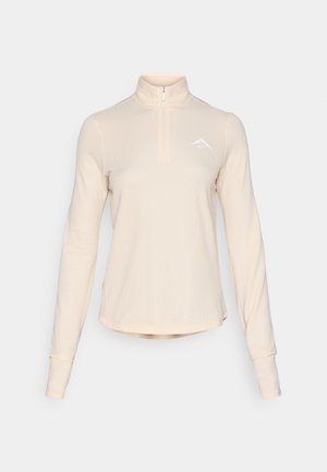 Lys beige langermet topp med viert zip, laget av teksturert stoff, med en liten hvit logo på brystet og tettsittende mansjetter.