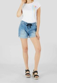 Valkoinen t-paita, jossa on monivärinen "CREATE" -printti, yhdistettynä sinisiin farkkushortseihin, joissa on naru vyötäröllä ja käärityt lahkeet, sekä mustiin korkokenkiin.