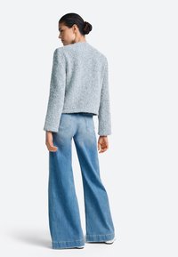 Világoskék texturált, rövidített hosszú ujjú dzseki, széles szárú világos farmerrel párosítva. Az öltözet laza, kényelmes szabású.