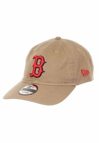 Khaki baseball cap with red and navy embroidered "B" logo. Features a curved brim, adjustable strap, and fabric texture. New Era branding tag included.