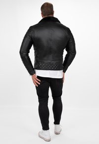 Zwarte leren jas met een doorgestikte patroon op de onderrug en mouwen. Heeft een bontgevoerd kraag en een slim-fit ontwerp.