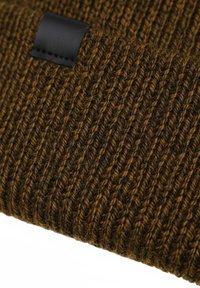 Cappello lavorato a maglia in lana marrone scuro con motivo a coste testurizzato e etichetta di pelle nera come dettaglio. Vista ravvicinata del dettaglio del tessuto.