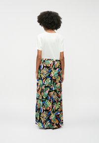 Jupe maxi avec un motif de feuilles tropicales multicolores sur fond noir. Associée à un tee-shirt blanc à manches courtes uni. Tissu en mélange de coton.