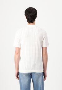 Hvid kortærmet striktop med ribbet tekstur og runde halsudskæring. Bagsiden præsenterer en ren, minimalistisk stil uden yderligere detaljer.