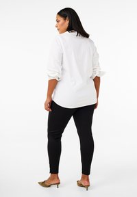 Valge pika varrukaga särk koos rullitud varrukatega, kombineeritud mustade retuusidega, millel on külg nupud, ning oliivroheliste kontsakingadega.