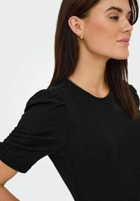 Top nero a righe con maniche a bufalo corte. Presenta un colletto rotondo e una sottile texture. Una collana in oro mette in risalto il colletto.