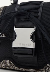 Sac à main noir en nylon texturé, avec des accessoires en métal argenté et une boucles métallique imposante. Présente un motif clouté le long du bord inférieur.