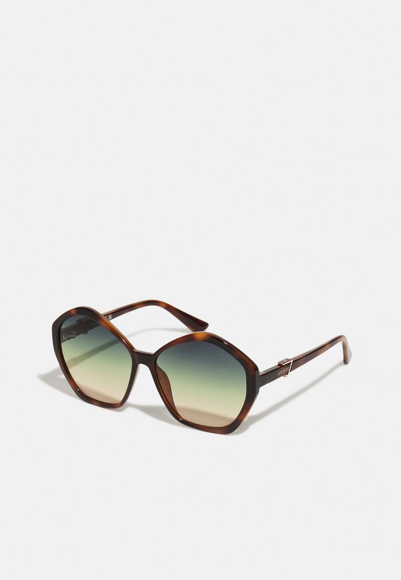 Ochelari de soare tortoiseshell maro cu un cadru larg, unghiular și lentile cu gradient care trec de la întunecat la deschis, având accente metalice.