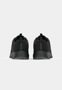 Schwarze Sportschuhe mit einem Obermaterial aus Mesh, abgerundeter Zehenform und strukturiertem Sohlen. Mit einem Zugband auf der Rückseite und dezentem Branding an der Seite.