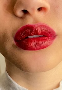 Matte red lipstick on full lips, showcasing texture and a gradient effect toward the center. Smooth skin and a neutral background.