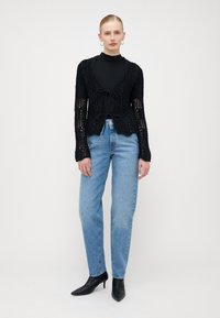 Μαύρο πλεκτό cardigan με v-λαιμόκοψη, ανοιχτό μπροστινό μέρος και λεπτομέρεια με κορδόνι. Συνδυασμένο με ανοιχτόχρωμο μπλε τζιν με ευθεία γραμμή και μαύρες μυτερές γόβες.