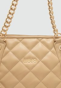 Beige handtas met quilted ontwerp en een gouden kettingstrap. Voorzien van een opvallend merlogo en een soepele leren textuur. Kenmerkend ontwerp met een diamantpatroon.