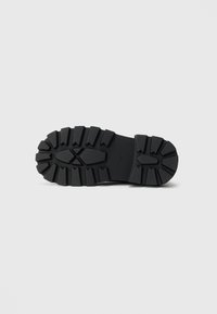 Black rubber shoe sole with a textured tread pattern, featuring deep grooves for traction and a solid, flat design.